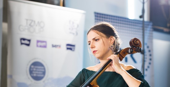 kobieta grająca na wiolonczeli, w tle znak firmowy mecenasa