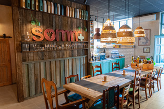 stolik z krzesłami, w tle lada z produktami, na drewnianej ścianie logotyp sklepu SOMM+