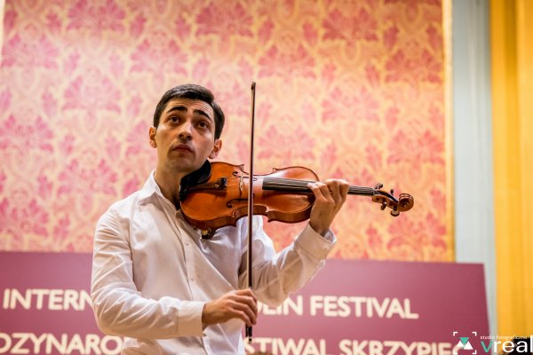 mężczyzna gra na skrzypcach za nim baner z nazwą festiwalu