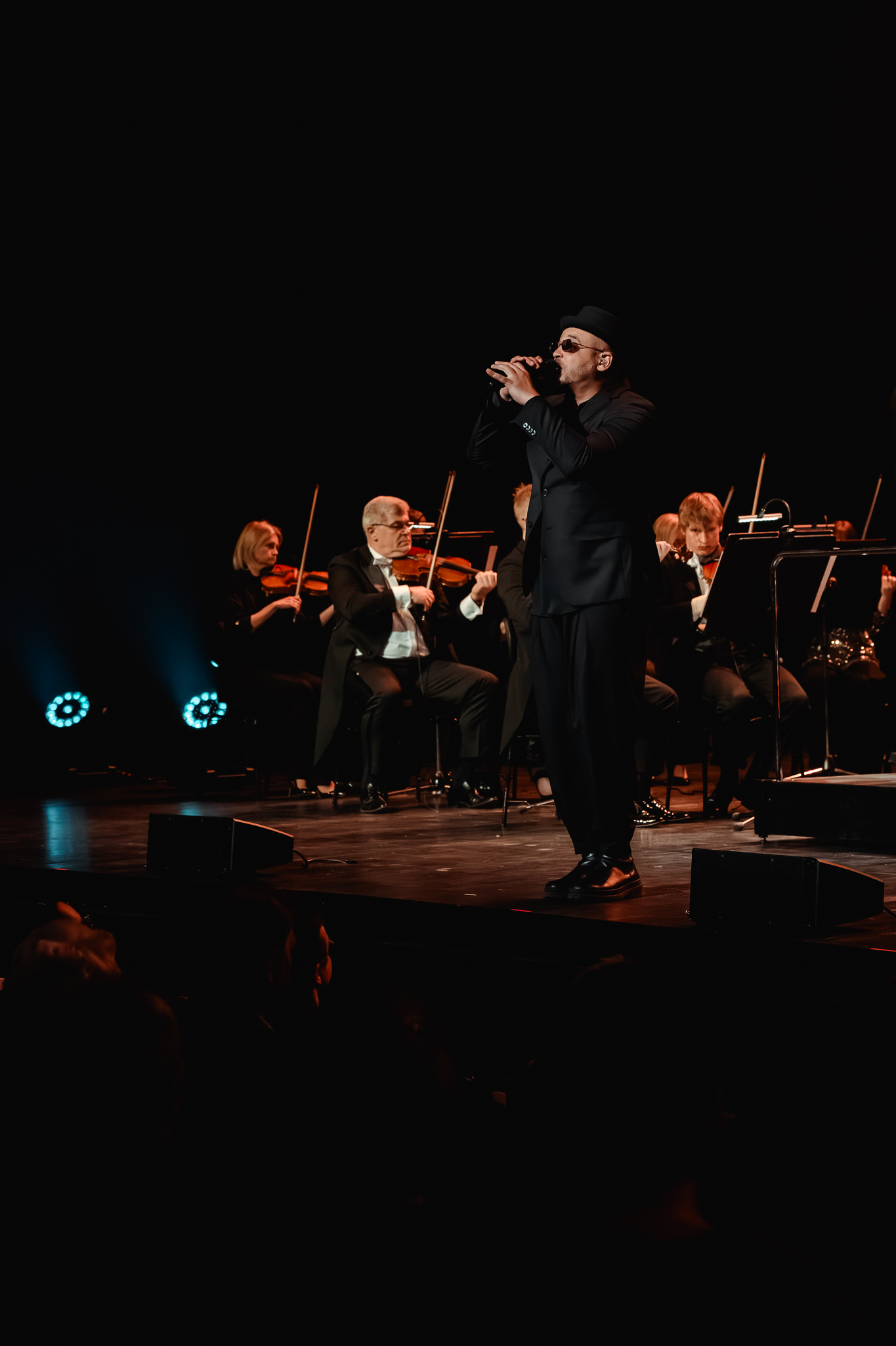 mężczyzna śpiewający do mikrofonu, w tle siedzi orkiestra