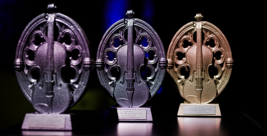 trzy statuetki o owalnym kształcie w środku ze skrzypcami, z lewej strony dwie w kolorze srebrnym, od prawej jedna w kolorze złotym