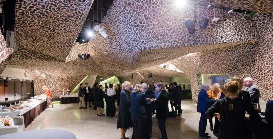 bankiet po koncercie na dolnym foyer, Kontrahenci, Mecenasi ubrani w strojach wieczorowych, trzymają kieliszki z szampanem przy stolikach bankietowych