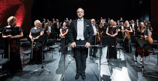 Mężczyzna we fraku stojący przed orkiestrą