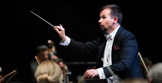 mężczyzna we fraku z batutą i uniesioną ręką