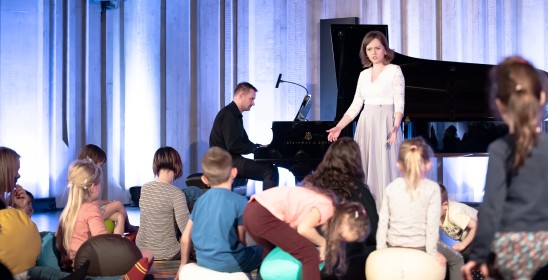 stojąca kobieta i dzieci siedzące na dywanie