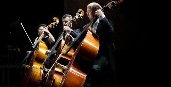 trzech muzyków grających na wiolonczelach