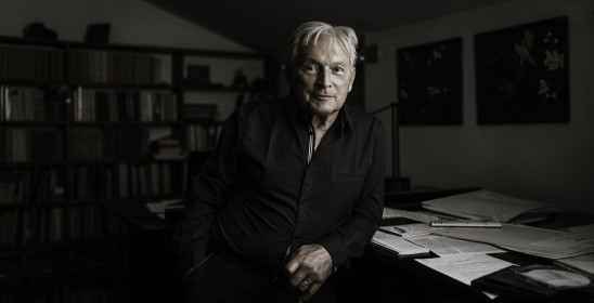 mężczyzna w ciemnej koszuli opierający się o stolik z rozłożonymi zapisami nutowymi