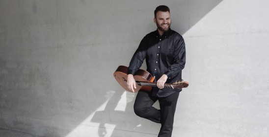 stojący mężczyzna opierający się o ścianę, trzyma gitarę