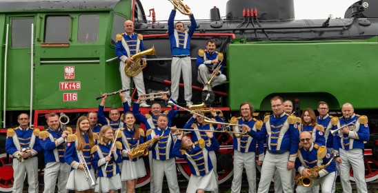 człoknowie orkiestry dętej na tle starej lokomotywy