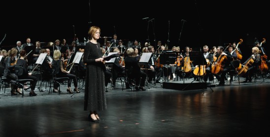 kobieta mówiąca do mikrofonu, w tle orkiestra na scenie