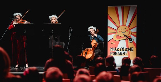 troje muzyków grających na scenie, po prawej stronie rollup z grafiką muzycznych poranków