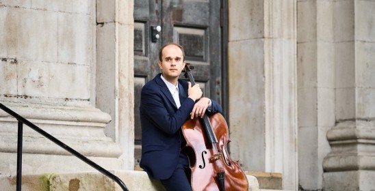 siedzący mężczyzna trzyma wiolonczelę