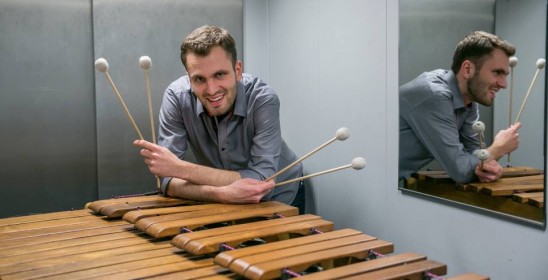 mężczyzna trzymający pałeczki do gry opiera się o marimbę