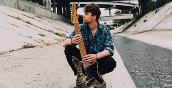 siedzący mężczyzna trzyma w rękach gitarę elektryczną