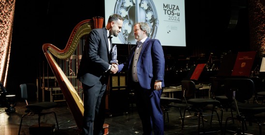 dwóch mężczyzn w garniturach przekazujących sobie statuetkę