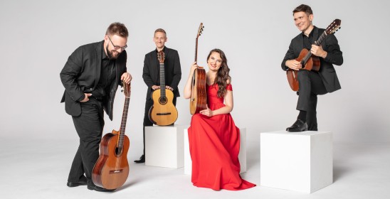 trzech elegancko ubranych gitarzystów oraz gitarzystka ubrana w czerwoną długa suknię