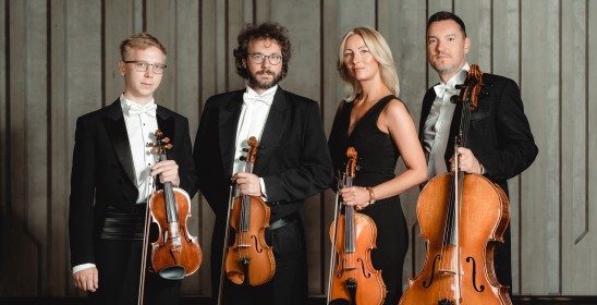 czworo muzyków stoi i pozuje do zdjęcia, pierwszy trzyma skrzypce, drugi skrzypce, trzecia altówkę, czwarty wiolonczelę