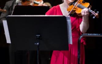 Kobieta z blond włosami w czerwonej sukni gra na skrzypcach