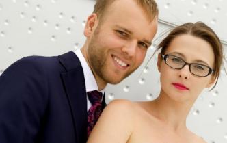 uśmiechnięty mężczyzna w garniturze stoi za kobietą w okularach 
