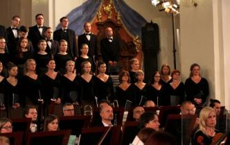 chór mieszany ubrany na czarno w przestrzeni kościoła, przed nimi część orkiestry
