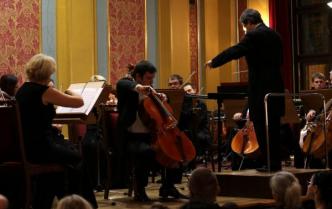 na pierwszym planie solista gra na wiolonczeli w tle orkiestra