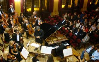 solista gra na fortepianie za nim dyrygent i część orkiestry przed nim publiczność zdjęcie robione z góry