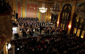 orkiestra siedzi na scenie, za nimi chóry, widok na głowy publiczności z tyłu z balkonu