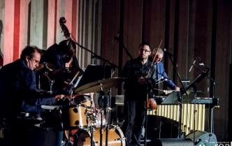 czterej mężczyźni stoją na scenie przy instrumentach, na pierwszym planie zestaw perkusyjny