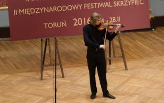 mężczyzna w czarnym stroju gra na skrzypcach na scenie, za nim baner z nazwą festiwalu