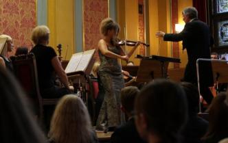 solistka na scenie gra na skrzypcach obok dyrygent i orkiestra