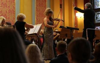 solistka na scenie gra na skrzypcach obok dyrygent i orkiestra