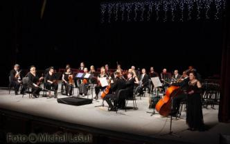 orkiestra siedzi na scenie na czarnym tle w nastrojowym świetle