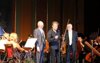trzej starsi mężczyźni na scenie w miejscu solistów, jeden z nich trzyma skrzypce i przemawia do mikrofonu
