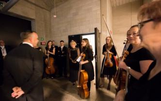 uśmiechnięci muzycy kobiety i mężczyźni wraz z dyrygentem stoją przed wejściem na scene