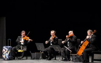 czterej mężczyźni w czarnych frakach siedząc grają na instrumentach smyczkowych
