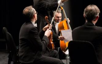 na scenie czterej mężczyźni we frakach z instrumentami smyczkowymi jeden z nich stoi z rozłożonymi rękoma