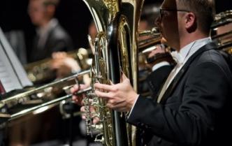 mężczyzna gra na tubie za nim zamazani inni muzycy 