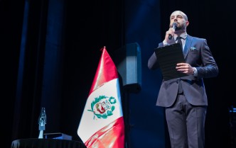Mężczyzna mówiący do mikrofonu obok flagi Peru