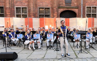 a man speaking into a microphone, behind him is a brass band