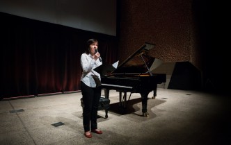 a woman speaking into the microphone, behind her is a piano
