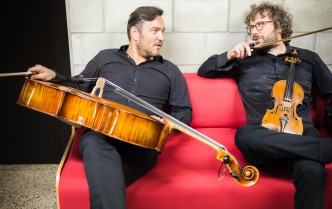 two men sitting on the couch holding a cello and violin