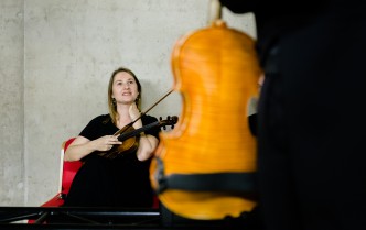 siedząca kobieta trzyma skrzypce, na pierwszym planie widoczne pudło rezonansowe skrzypiec