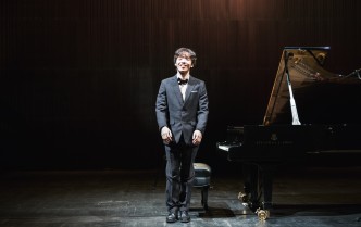 uśmiechnięty młody mężczyzna w ciemnym garniturze stoi obok fortepianu