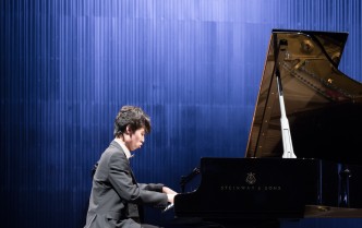 na scenie sali kameralnej młody mężczyzna w ciemnym garniturze gra na fortepianie