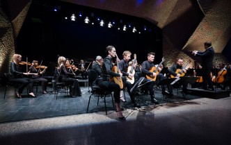 czworo gitarzystów, w tle siedzi orkiestra