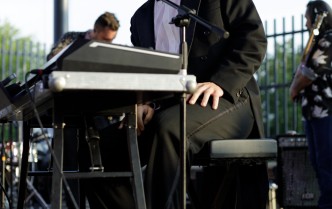 mężczyzna w garniturze siedząc przy elektrycznym pianinie śpiewa do mikrofonu