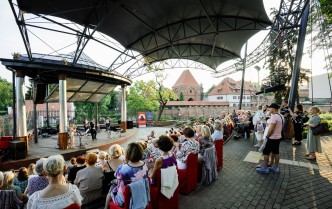 publiczność koncertu ukazana od tyłu z widokiem na scenę amfiteatru i znajdujących się na niej wykonawców