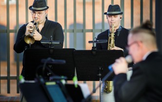 dwaj mężczyźni w ciemnych koszulach i czarnych kapeluszach grający na trąbce i saksofonie
