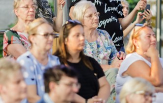 publiczność koncertu ukazana z dołu do góry, najwyżej osoby trzymają plakat z nazwą zespołu