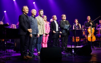 grupa ośmiu muzyków stojąca razem na scenie na zakończenie koncertu